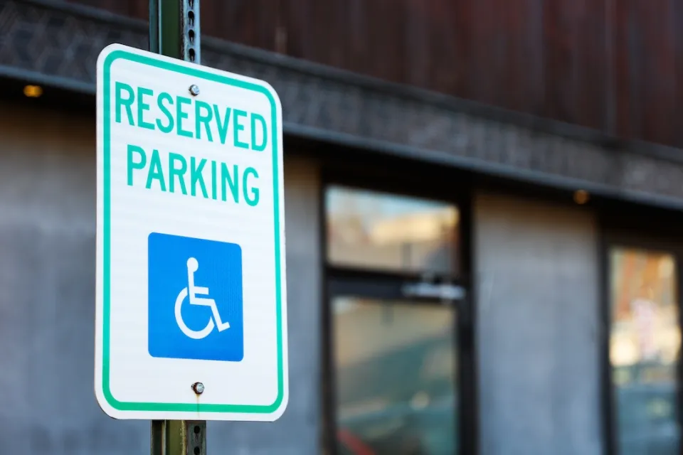 Close-up on white sign with green "Reserved Parking" letters and blue accessibility symbol.